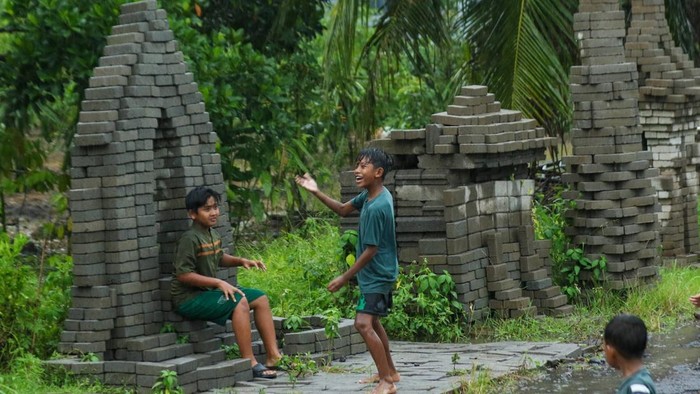 Sejumlah anak-anak bermain di area candi paving di Desa Sembulungan, Cluring, Banyuwangi, Jawa Timur, Minggu (8/2/2026). Sebanyak 13 bangunan menyerupai candi yang terbuat dari bahan paving material proyek pembangunan jalan yang tak kunjung dikerjakan itu dibangun warga menjadi karya seni dan bentuk protes karena menyebabkan penyempitan dan mengganggu pengguna jalan. ANTARA FOTO/Budi Candra Setya