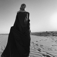 Dengan latar gurun pasir, Agnez Mo tampak mengenakan abaya cokelat berbahan satin dengan train panjang. Foto: Instagram/@agnezmo