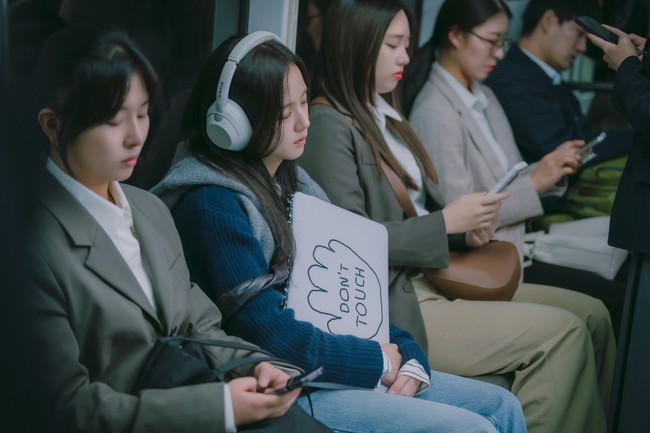 Dalam foto terbaru yang dirilis, Jisoo BLACKPINK bertransformasi sebagai Seo Mi Rae, terlihat lelah saat melakukan perjalanan ke kantor. Pakai headphone, ketiduran, sampai memegang sign “Don’t Touch” agar waktu istirahatnya tak terganggu. Foto: dok. Netflix