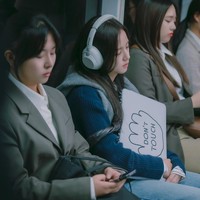 Dalam foto terbaru yang dirilis, Jisoo BLACKPINK bertransformasi sebagai Seo Mi Rae, terlihat lelah saat melakukan perjalanan ke kantor. Pakai headphone, ketiduran, sampai memegang sign “Don’t Touch” agar waktu istirahatnya tak terganggu. Foto: dok. Netflix