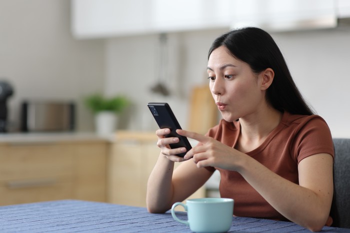 Surprised asian woman using smart phone in a kitchen at home