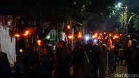 Deretan obor bambu yang menyala membentuk garis cahaya memanjang, mengiringi langkah para peserta sepanjang rute pawai.