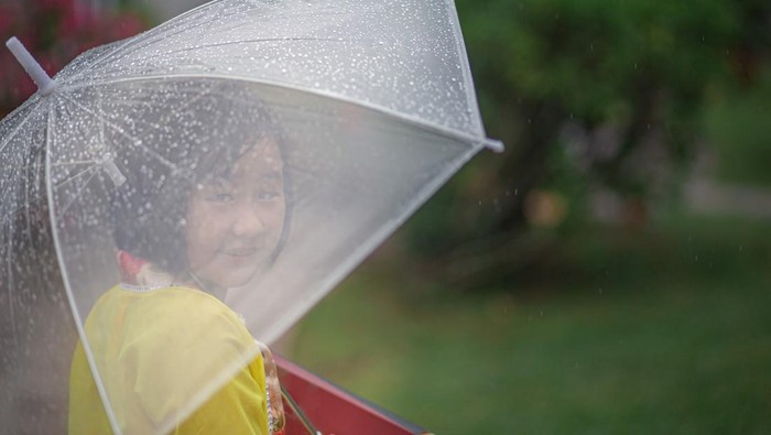 Asia Chinese girl holding umbrella and moon cake box walking in public park rainy day. She enjoying mid-autumn festival.