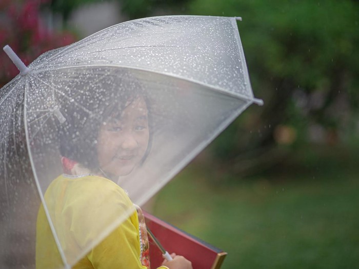 Asia Chinese girl holding umbrella and moon cake box walking in public park rainy day. She enjoying mid-autumn festival.