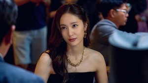 Penampilan Jeon Yi Kyung yang mewah dan glamour dngan dress hitam dan perhiasan emas berbentuk mata rantai besar-besar. (Foto: dok. tvN)