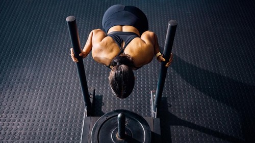 Female athlete pushing a weighted sled in a gym. Top view of a woman performing strength training exercise on a black gym floor. Hyrox Training Concept.
