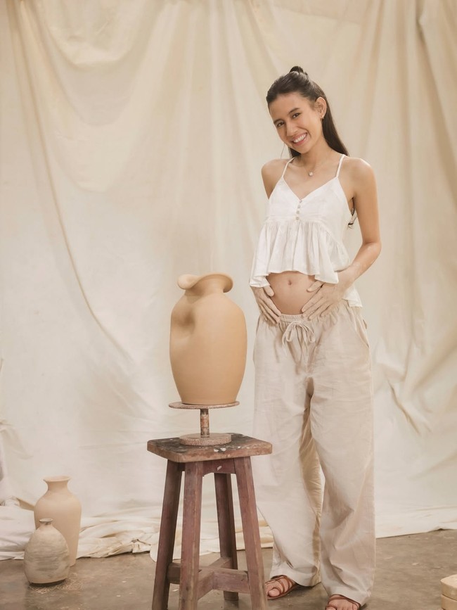 Dalam maternity shoot kali ini, Shenina mengenakan flare crop top warna putih dan celana panjang khaki yang kasual. Bahkan hanya dilengkapi sandal gladiator yang sederhana namun manis. Foto: Dok. Instagram Shenina Cinnamon