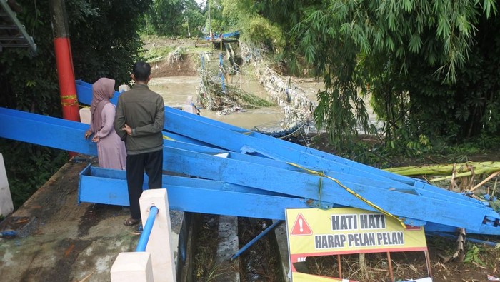 Warga mengamati jembatan gantung Darus atau Jembatan Cinta yang terputus akibat banjir di Desa Jubung, Sukorambi, Jember, Jawa Timur, Sabtu (14/2/2026). Jembatan penghubung Kecamatan Sukorambi dan Ajung tersebut terputus akibat banjir pada Kamis (12/2) yang mengakibatkan warga harus menggunakan rute lain sejauh tujuh kilometer dari sebelumnya satu kilometer. ANTARA FOTO/Seno.