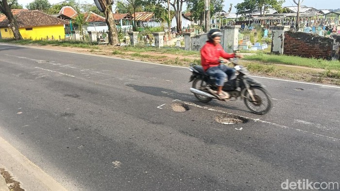 Seorang pengendara melintasi sebelah lubang yang ada di Jalan Pantura Desa Larangan, Kecamatan Lohbener, Kabupaten Indramayu, Sabtu (14/2/2026).