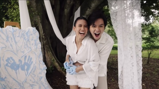 Serasi dengan sang istri, Angga juga mengenakan kemeja putih. Kemeja putih lengan pendek tersebut dipadukan dengan celana panjang bahan warna nude. Foto: Instagram/@sheninacinnamon