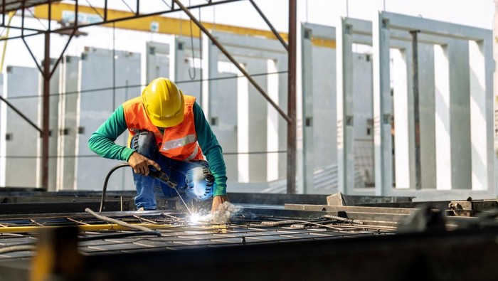 Workers at a construction site weld metal structures of precast concrete slabs.