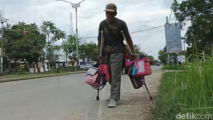 Eryana menggendong tas dan berjalan dengan kruk menjajakan barang dagangannya kepada warga setempat, di Jalan Gatot Subroto Indramayu, Kamis (19/2/2026).