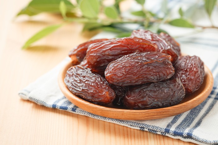 Date fruit in wood bowl on placemat, Dried date palm fruits top view