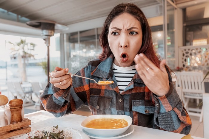 Young woman sitting at an outdoor cafe, surprised by the heat and piquancy of her soup, showcasing a humorous dining experience