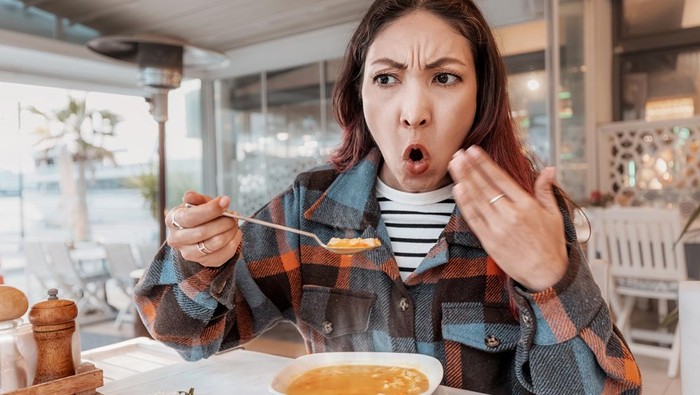 Young woman sitting at an outdoor cafe, surprised by the heat and piquancy of her soup, showcasing a humorous dining experience