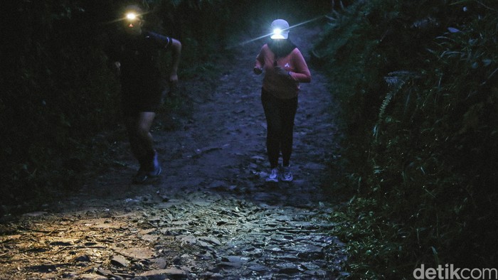 Jalur trail Cisadon di Bojong Koneng, Bogor, kian diminati pelari Jabodetabek berkat medan variatif, elevasi menantang, dan suasana desa yang masih alami.
Jalur trail Cisadon di Bojong Koneng, Kabupaten Bogor, semakin populer sebagai lokasi latihan lari trail bagi pelari Jabodetabek. Aksesnya yang relatif dekat dari kawasan perkotaan serta karakter medan yang bervariasi menjadikan jalur ini cocok untuk pelari pemula hingga berpengalaman yang ingin melatih daya tahan dan berburu elevasi di alam terbuka.
Sejumlah pelari rutin memanfaatkan jalur ini untuk latihan berkala, bahkan memulai aktivitas sejak dini hari. Salah satunya Eko, karyawan swasta asal Jakarta, yang bersama rekan-rekannya hampir setiap bulan berlari di Cisadon. Rute dari area sekitar kandang sapi milik Presiden Prabowo Subianto menuju Desa Cisadon dapat mencapai sekitar 7 kilometer sekali jalan, dengan jarak tempuh yang bisa bertambah sesuai jalur dan menu latihan.
Di sepanjang rute, papan penunjuk arah membantu pelari dan pendaki menuju berbagai destinasi lain seperti Bukit Paniisan, Situ Rawa Gede, Pasir Limo, hingga jalur yang terhubung ke Gunung Pancar dan kawasan Puncak. Jalur trekking Cisadon juga menawarkan banyak spot foto menarik dengan latar sawah, kebun teh, hutan pinus, sungai, dan perbukitan yang terbuka luas, termasuk panorama dari Bukit Pasir Limo yang menampilkan lanskap Bogor dari ketinggian.
Namun, karakter jalur yang berupa jalan desa rusak, tanah, makadam, serta lintasan anak sungai dan kubangan menghadirkan tantangan tersendiri, terutama saat musim hujan ketika jalur berubah menjadi licin dan berlumpur. Minimnya sinyal seluler serta suasana desa yang tenang dan alami justru menjadi daya tarik tambahan, menghadirkan pengalaman latihan yang menyatu dengan kehidupan warga lokal sekaligus kesempatan untuk sejenak lepas dari hiruk-pikuk dunia digital.