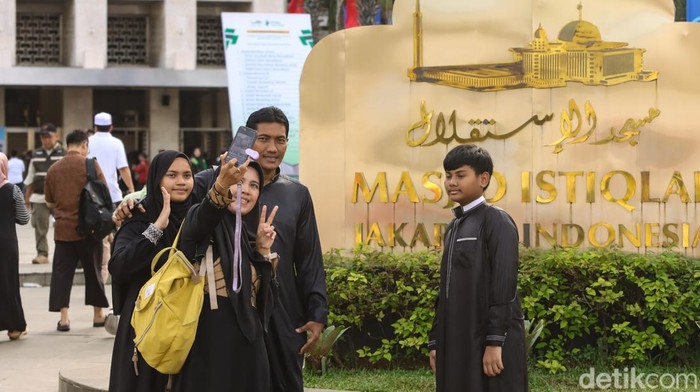 Warga berfoto di depan papan nama Masjid Istiqlal, Jakarta, menjelang berbuka puasa. Area ini menjadi spot favorit keluarga untuk mengabadikan momen Ramadan.