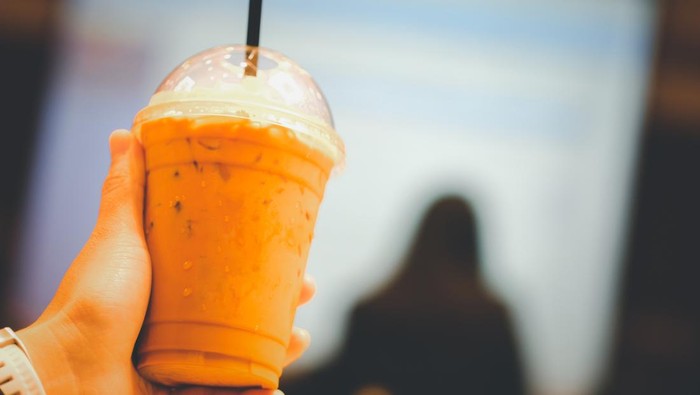 Hand holding a glass of cold Thai milk tea in meeting room
