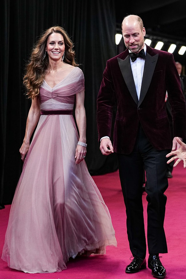 Pangeran William tampil serasi dalam balutan Emporio Armani Velvet Evening Jacket berwarna merah gelap, senada dengan ikat pinggang yang dikenakan Kate. Foto: BAFTA via Getty Images/Scott Garfitt