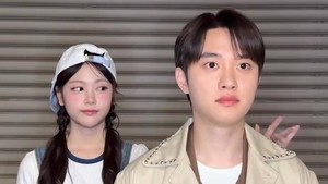Carmen berdiri di belakang D.O.EXO lalu nyolek pundak kiri seniornya di SM Entertainment itu. Pas D.O. noleh, Carmen pura-pura gak ngapa-ngapain. (Foto: dok. Instagram @hearts2hearts)