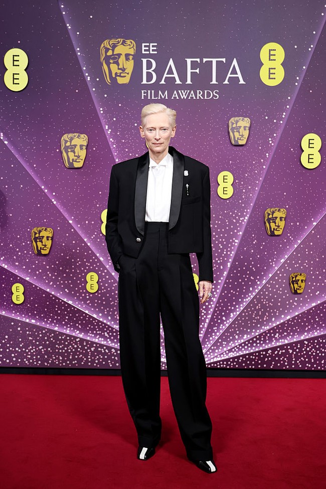 Salah satu tampilan paling mencuri perhatian datang dari Tilda Swinton. Alih-alih mengenakan gaun, ia memilih setelan jas dari Chanel. Jaket tuksedo cropped, celana high-waisted, serta bahu tegas menciptakan proporsi yang kuat dan androgini, sekaligus menjadi pernyataan gaya berbeda di antara dominasi gaun malam. (Foto: Aurore Marechal/BAFTA/Getty Images for BAFTA)