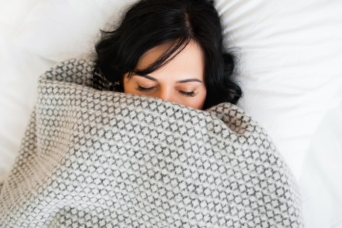 Sleeping woman cover face with blanket flat lay. Close-up of young brunette women, sleeping under gray blanket and covering half face. Almost fully covered sleeping girl