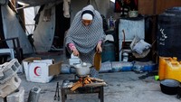 Seorang perempuan menyiapkan dan memasak hidangan untuk berbuka puasa di area terbuka bekas rumah mereka. Aktivitas itu dilakukan dengan peralatan terbatas. REUTERS/Mahmoud Issa