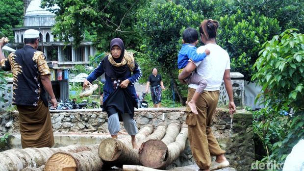 Momen warga dan lansia menyeberang sungai lewat jembatan darurat batang pohon kelapa di Kecamatan Lembar, Lombok Barat, NTB, Rabu (25/2/2026).