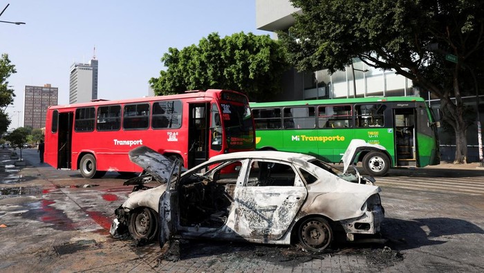Police officers and civilians walk near the burned wreckage of a vehicle used as a barricade by members of organized crime, following a series of detentions by federal forces, in Guadalajara, Mexico, February 22, 2026. REUTERS/Michelle Freyria  REFILE - UPDATING SLUG