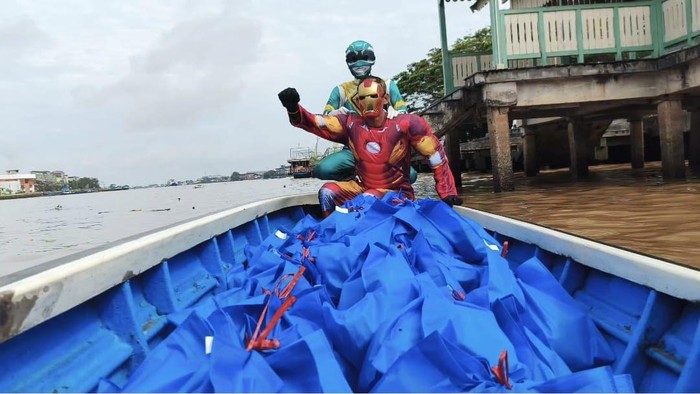 Dua petugas mengenakan kostum superhero mengarungi sungai untuk mengantar MBG ke sekolah yang sulit dijangkau jalur darat. (dok Istimewa)