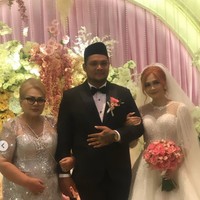 Ibunda Virgoun, Eva Manurung, memilih kenakan dress panjang abu-abu dengan model bagian atas sheer. Ia berpose bertiga bersama kedua mempelai. Foto: Instagram/@virgoun_/@lindifitriyana