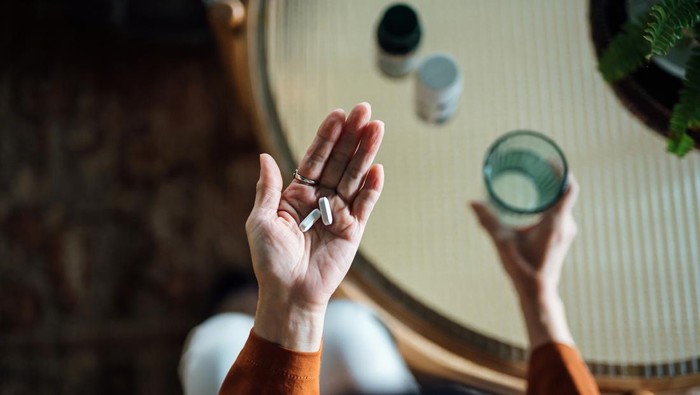 Overhead view of senior Asian woman feeling sick, taking medicines in hand with a glass of water at home. Elderly and healthcare concept