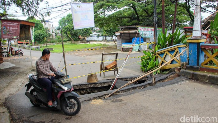 Pengendara motor melintas di ruas jalan ambles dekat Waduk Tiu Setu, Jalan Kampung Kramat Cipayung, Senin (2/3/2026).