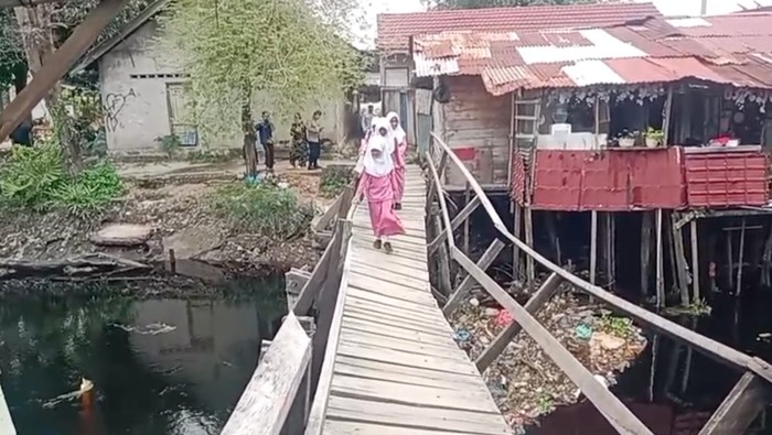 Anak-anak sekolah berjalan di jembatan miring di Gang Sungai, Kelurahan Bukit Datuk, Kecamatan Dumai Selatan, Kota Dumai, Jumat (6/3/2026).
