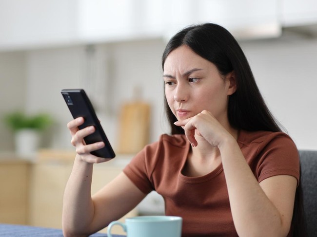 Suspicious asian woman checking phone content in the kitchen at home