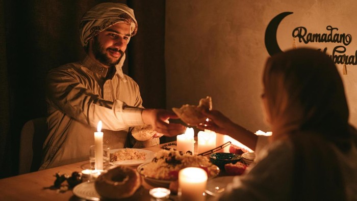 Jadwal buka puasa Jogja hari ini 7 Maret 2026. Dua orang bersiap menyantap hidangan di atas meja yang diterangi cahaya lilin.