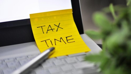Note berwarna kuning bertuliskan Tax Time di atas laptop.