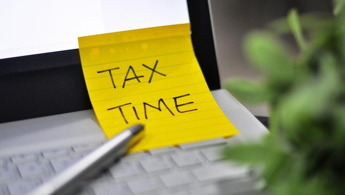 Note berwarna kuning bertuliskan Tax Time di atas laptop.