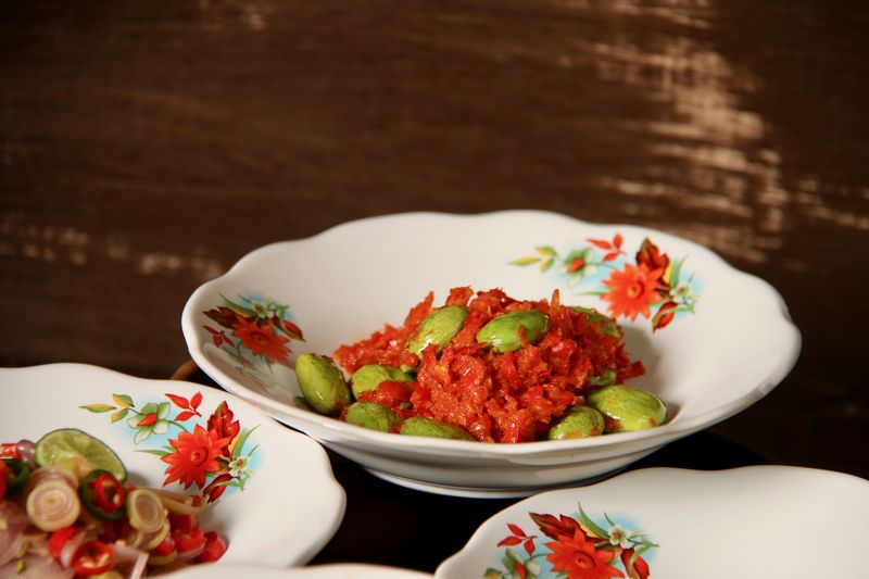 1040739016 Sambal Petai, a popular condiment of red chili paste with stink (bitter) beans from Central Java. The condiment is plated on old-fashioned crockery with red flowers paintings. It is served together with other popular spicy condiments from several other regions in Indonesia.