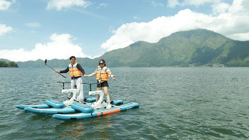 Dua pengunjung sedang berswafoto dengan latar belakang Gunung Abang saat bermaim sepeda air di Danau Batur, Bangli, Minggu (8/3/2026). (Aryo Mahendro/detikBali)
