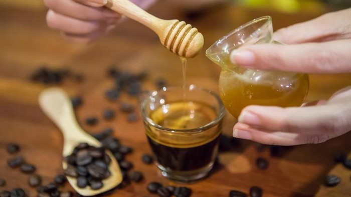 Woman hand pouring honey in a cup of coffee