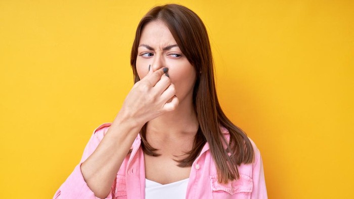 Girl pinched her nose with fingers, concept of unpleasant smell of sweat and bad breath, isolated in yellow studio