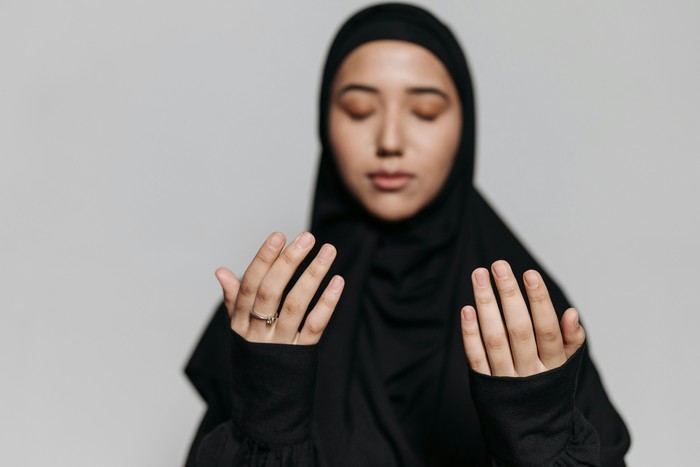 Seorang wanita yang mengangkat kedua tangannya, berdoa kepada Allah SWT.
