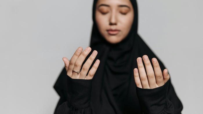 Seorang wanita yang mengangkat kedua tangannya, berdoa kepada Allah SWT.