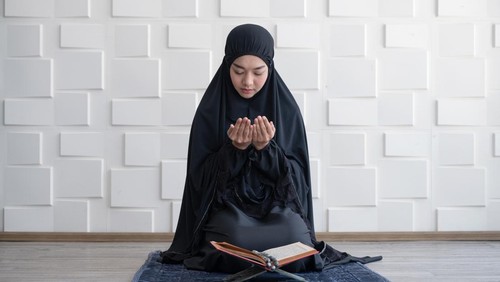 Muslim woman pray on hijab praying with Koran on mat indoors