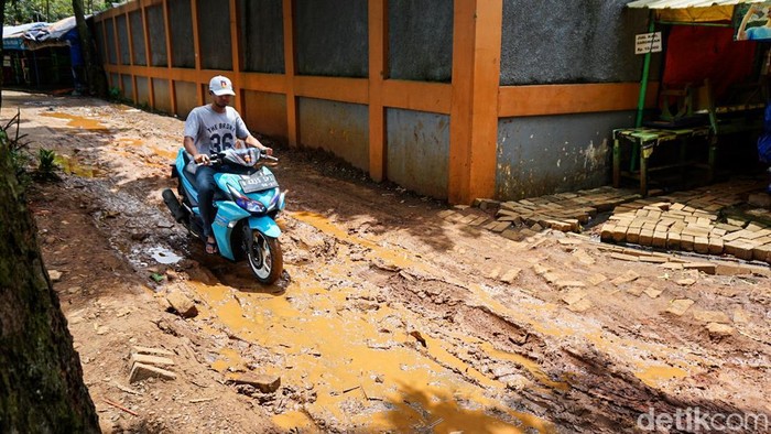 Kondisi salah satu ruas jalan yang mengelilingi waduk di kawasan Setu Babakan tampak mengalami kerusakan parah, Senin (9/3/2026). Permukaan jalan dipenuhi lubang yang digenangi air hujan bercampur tanah.