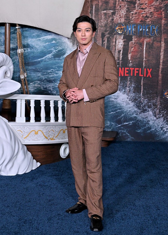 Mackenyu, pemeran Roronoa Zoro memilih gaya necis dengan setelan pin-stripe warna mocha dipadu kemeja satin beige dan pantofel. Foto: Getty Images