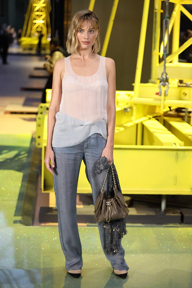 Atasan oversized itu dipadukan dengan celana denim longgar. Ia melengkapi tampilannya dengan sepatu high helles. perpaduan tan dan hitam. Aksesori yang dikenakan Robbie juga minimal. Ia membawa tas abu-abu Chanel rantai silver dan menggenggam scarf di tangannya.  Foto: WWD via Getty Images/WWD
