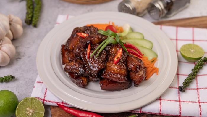 Sweet pork on a white plate with chopped scallions, chili, lime, cucumber, tomato, and garlic.
