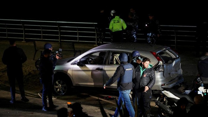 People gather next to a damaged car at the scene where a drone strike targeted another vehicle in Ramlet al-Baida at Corniche Beirut, following an escalation between Hezbollah and Israel amid the U.S.-Israeli conflict with Iran, in Beirut, Lebanon, March 12, 2026. REUTERS/Khalil Ashawi   REFILE - ADDING LOCATION